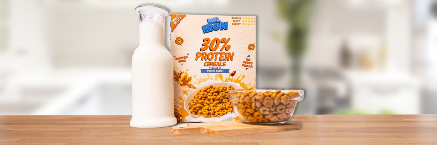 Cutie de cereale proteice Mr. Iron cu 30% proteine si aroma de unt de arahide, fara gluten sau zahar adaugat, alaturi de o sticla de lapte si un bol plin, pe un blat de bucatarie.